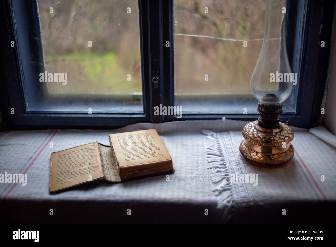 Ein altes offenes Buch auf einem Holztisch neben einer weißen Lampe, beleuchtet durch das warme gelbe Licht der Glühlampe Stockfoto