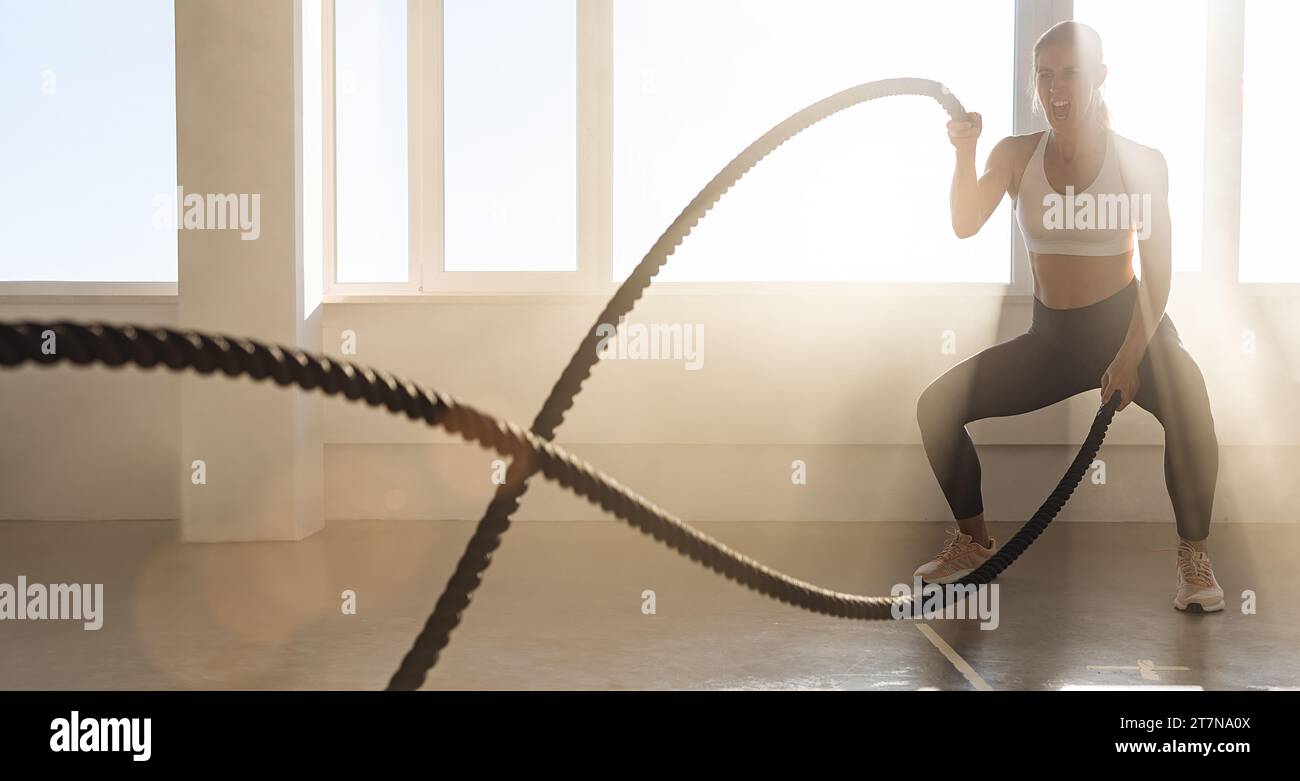 Junge athletische Frau mit perfektem Körper, die Crossfit-Übungen mit einem Seil im Fitnessstudio macht. Stockfoto