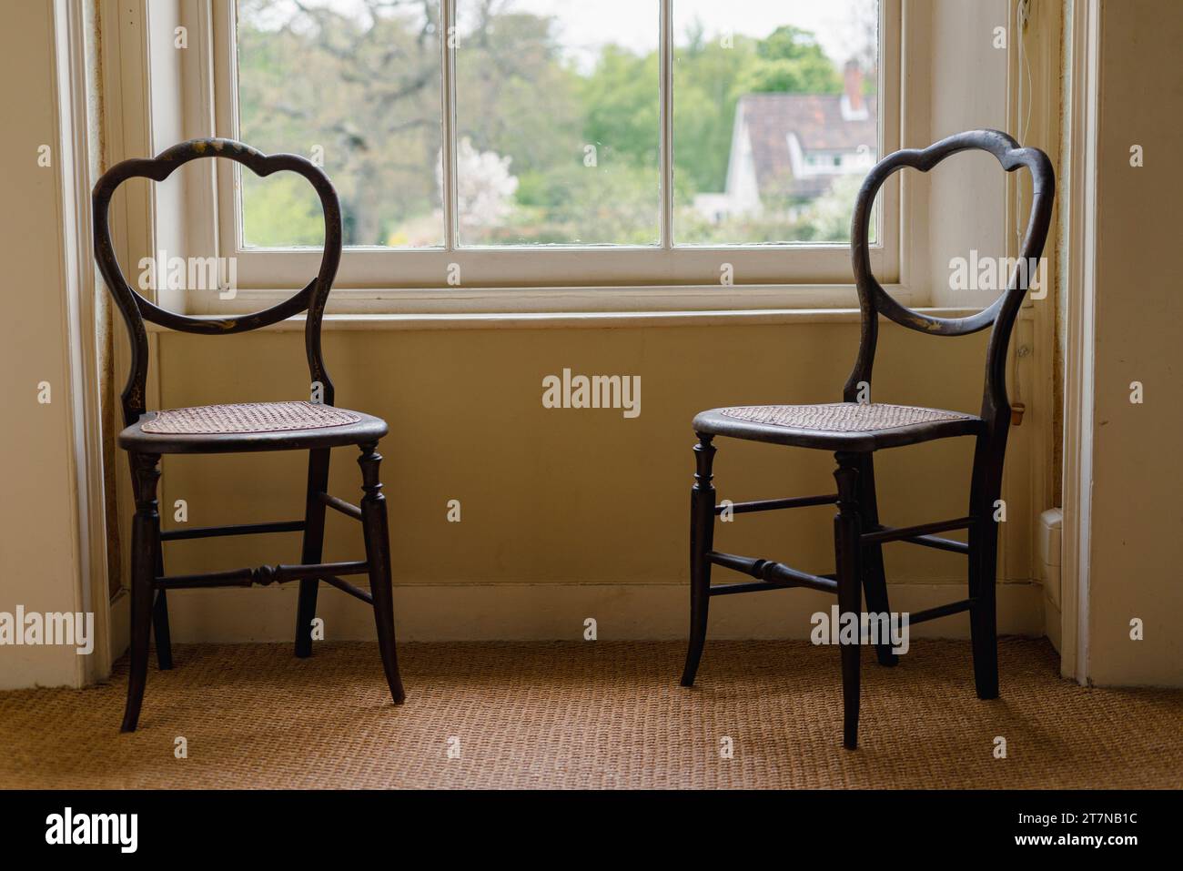 Zwei alte hölzerne Stühle sitzen vor einem großen Schiebefenster in einem großen Anwesen in Suffolk England in Großbritannien Stockfoto