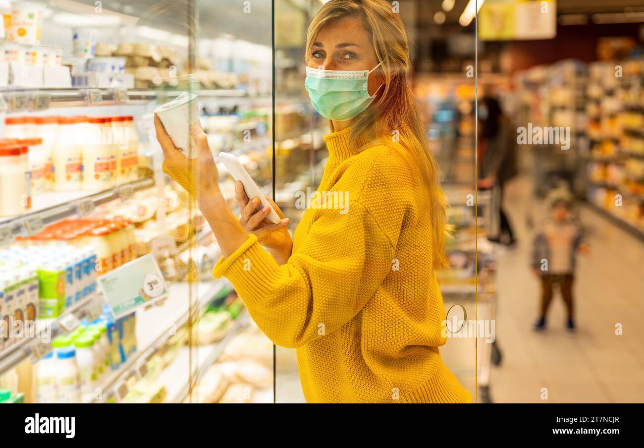 Frau in Maske, die während der COVID-19-Pandemie Joghurt im Lebensmittelgeschäft auswählt Stockfoto