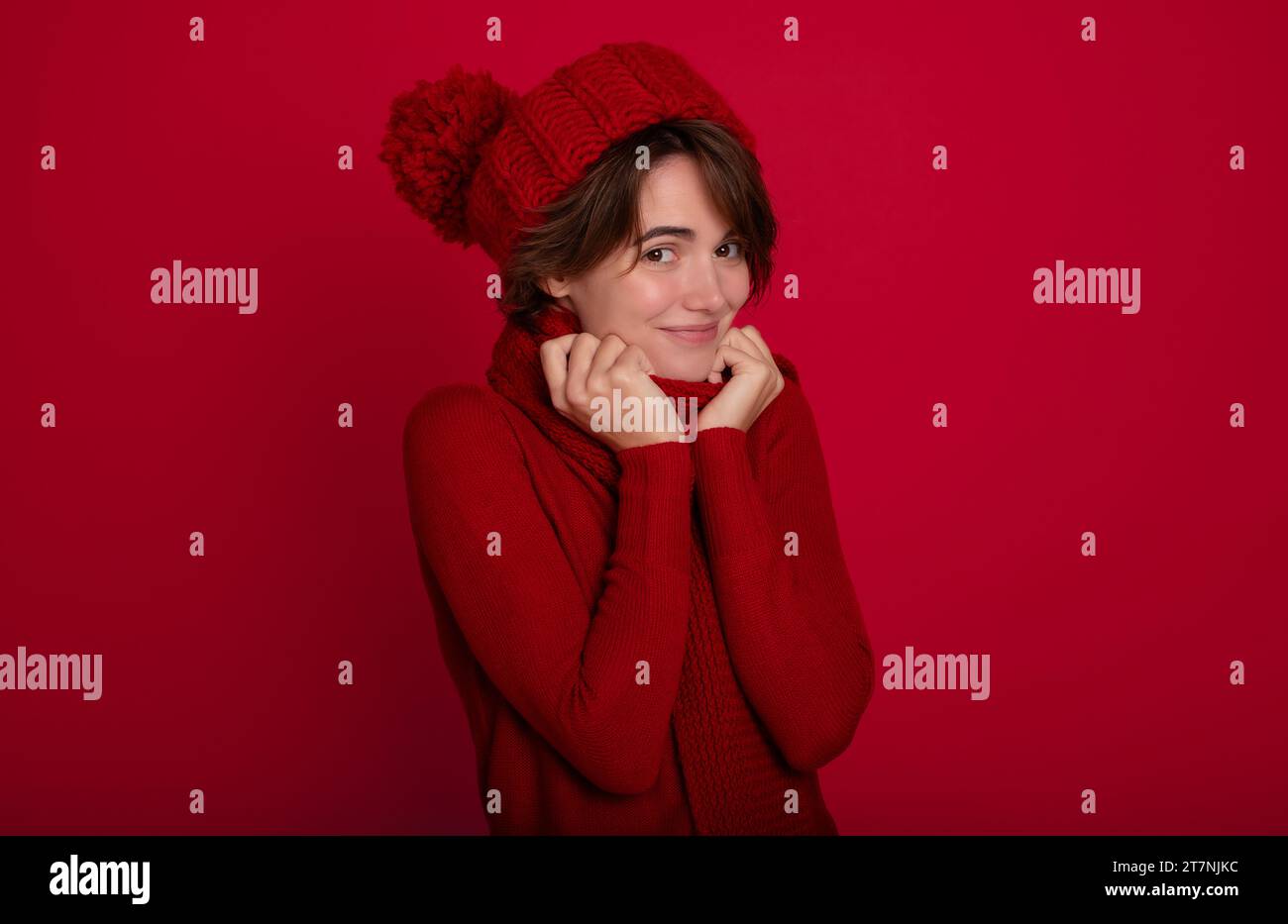 Nahaufnahme Porträt der lächelnden Frau in lässigem rotem Pullover und Wintermütze und Schal in guter Stimmung isoliert auf hellrotem Hintergrund. Werbung für Frauen Stockfoto