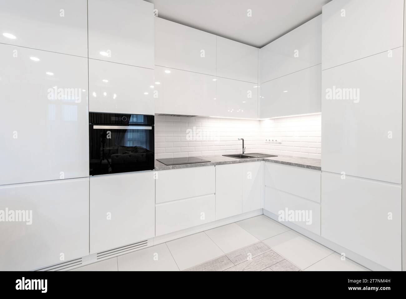 Moderne Inneneinrichtung. Küche mit Waschbecken und schwarzem Ofen. Weiße Möbel. LED-Leuchte. Luxuriöses Zuhause. Stockfoto