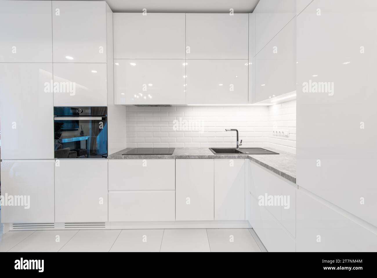 Moderne Inneneinrichtung. Küche mit Waschbecken und schwarzem Ofen. Weiße Möbel. LED-Leuchte. Luxuriöses Zuhause. Stockfoto