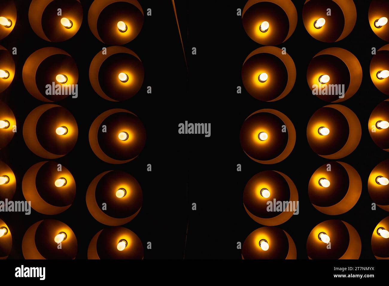 Blick auf die dunkle Decke des Korridors mit exklusiven und dekorativen Lampen mit kleinen Glühbirnen, die in dunkler Glaswand reflektiert werden Stockfoto