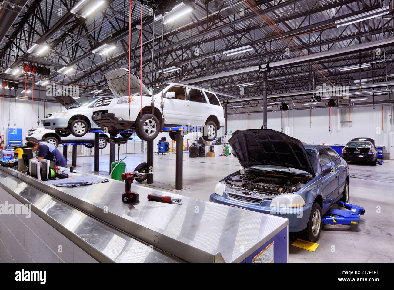 Hydraulische Hebebühnen heben Fahrzeuge an, um in einer modernen Werkstatt gewartet oder repariert zu werden Stockfoto