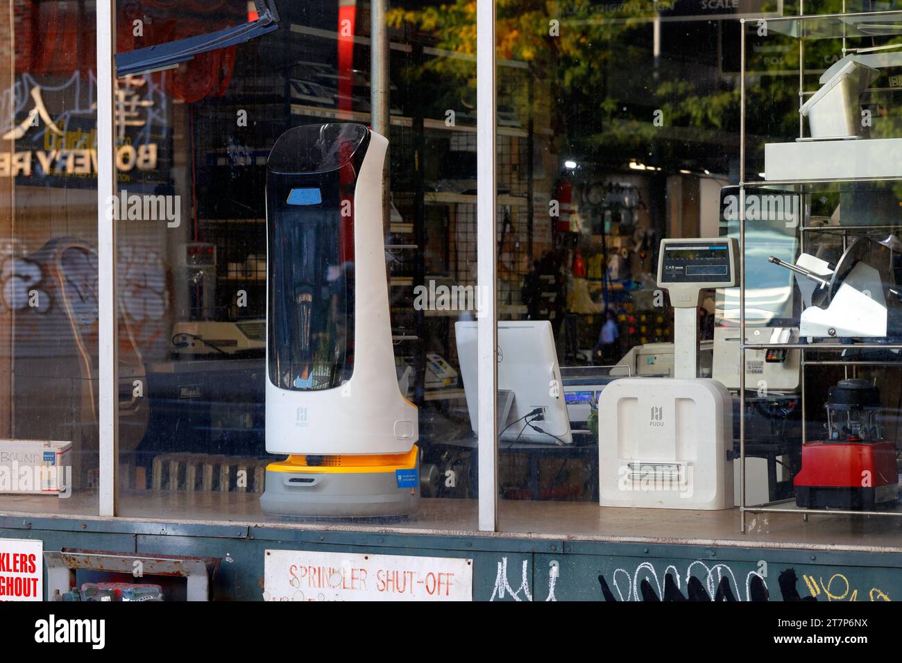 Ein Pudu Robotics Kettybot automatisierter intelligenter Lieferroboter, ein Retail Service Roboter, im Fenster eines Bowery Restaurant Supply Stores in New York City. Stockfoto