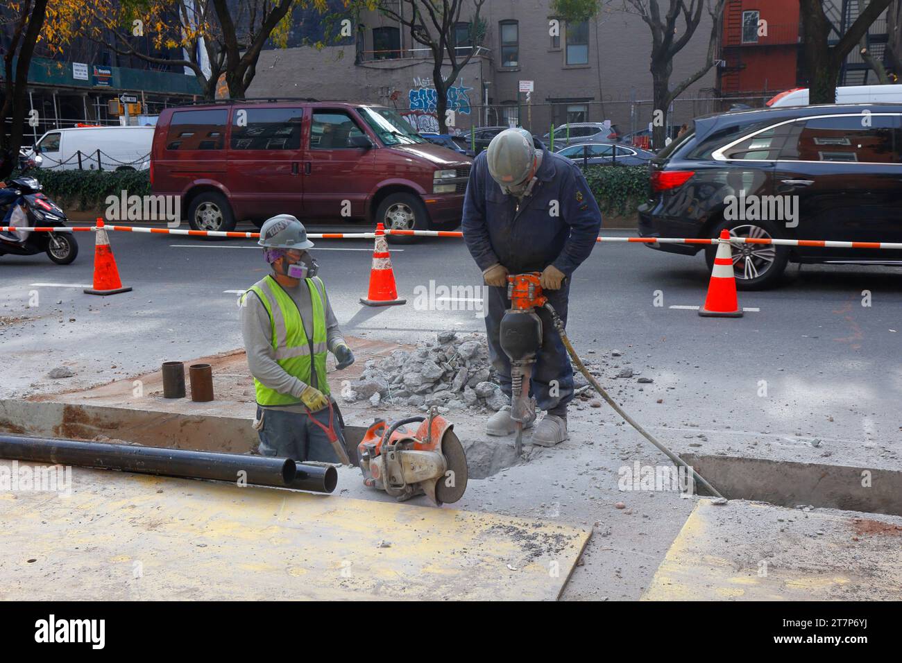 Eine Baumannschaft mit einem pneumatischen Schlaghammer zerbricht Beton für eine Straßenreparatur, während der Autoverkehr im Hintergrund steht. Stockfoto