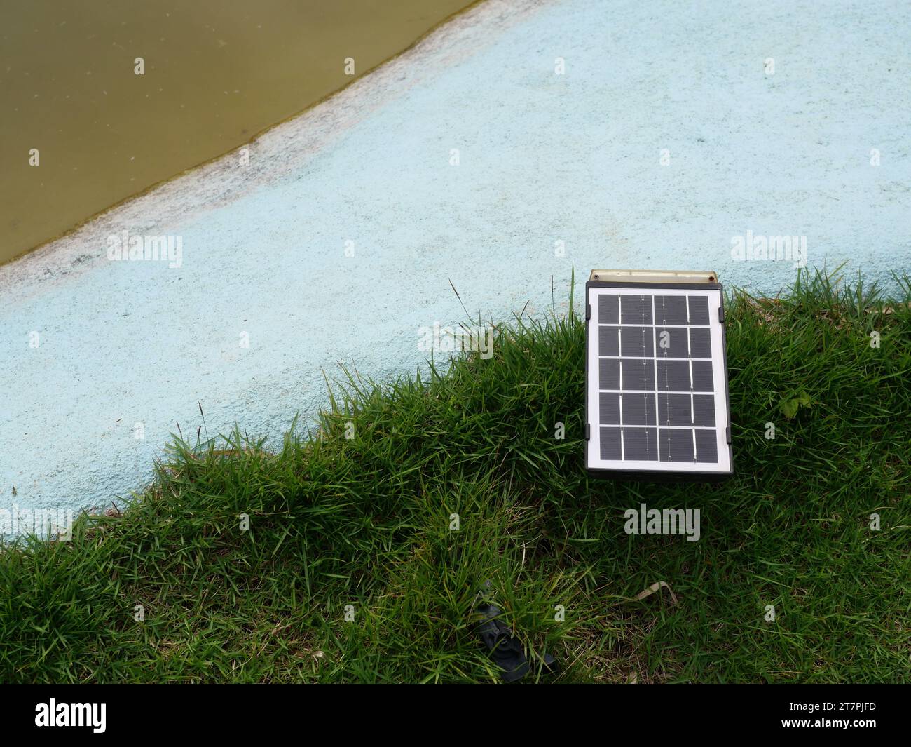 Kleines tragbares Solarzellenmodul auf dem Rasen am Teichrand, saubere Energie für die Stromerzeugung im Haus, mit alternativer Technologie Stockfoto