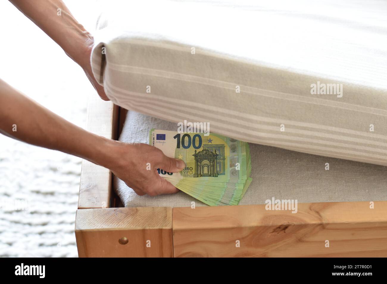 Eine Hand legt viele hundert Euro-Banknoten unter einer Matratze ein, was das Sparen in Bargeld symbolisiert Stockfoto