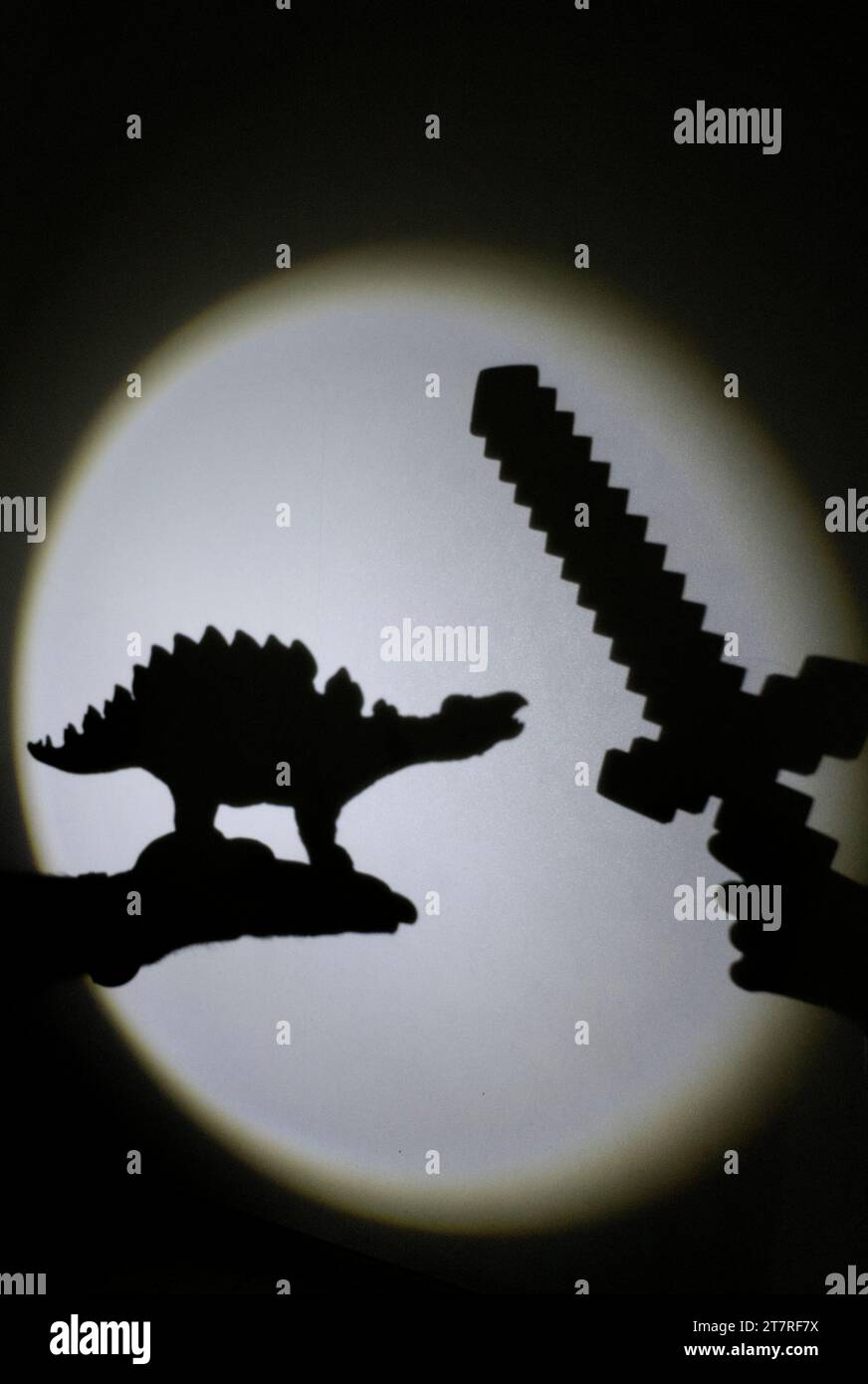 Interessante kontrastierende Schatten an der Wand von einem Spielzeug-Dinosaurier und einem Schwert. Stockfoto