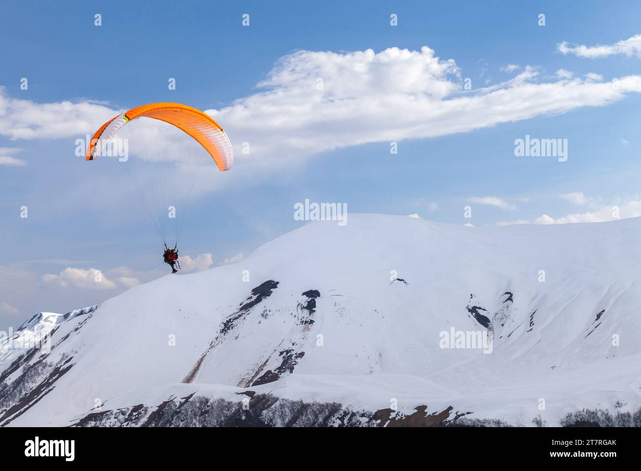 Gudauri, Georgia - 1. Mai 2019: Gleitschirmflieger fliegen an einem sonnigen Tag vor den verschneiten Gipfeln des Kaukasus Stockfoto