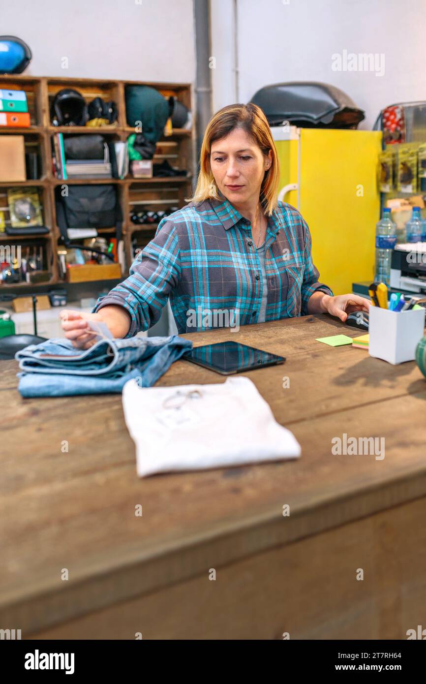 Die blonde junge Frau, die eine Jeansetikette aussieht, um den Preis im Laden zu überprüfen Stockfoto