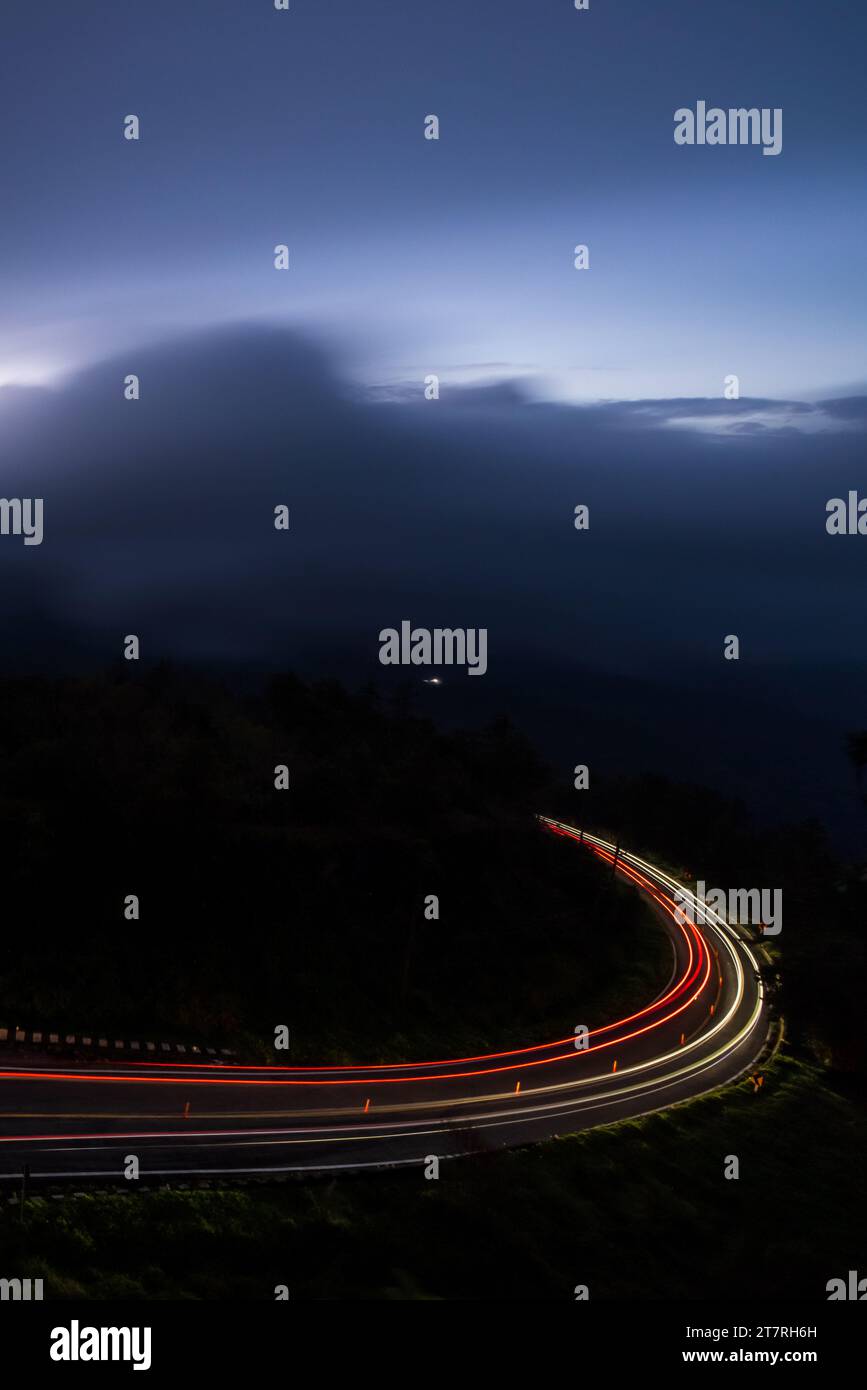 Fahren auf einer Bergstraße bei starkem Sturm, beleuchtete leichte Wege gegen dunkle Gewitter im Hintergrund. Transport, Reisekonzept Stockfoto
