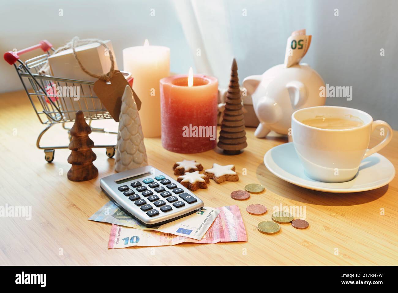 Sparen Sie Geld beim Einkaufen im Urlaub, Taschenrechner, Sparkasse, Münzen und Banknoten auf einem Tisch zwischen Weihnachtsdekoration, Kerzen und einem Einkaufswagen, Kopie Stockfoto