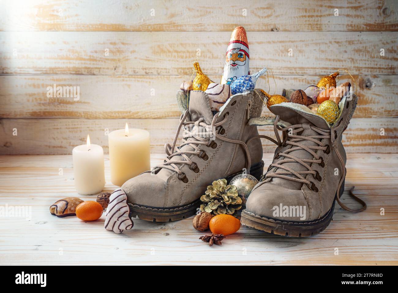 Winterstiefel, Süßigkeiten, Weihnachtsdekoration und ein Schokoladensmann gegen rustikales Holz, Tradition am Nikolaustag oder im deutschen Nikolaus Tag zum Füllen des Schuhs Stockfoto