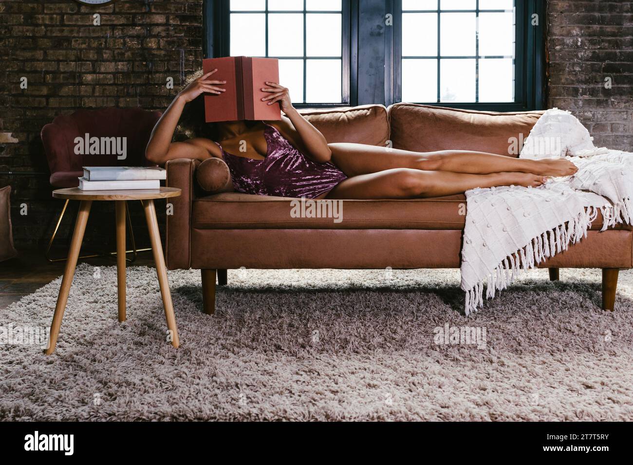Tänzerin in rosa Trikot auf der Couch und liest ein Buch Stockfoto