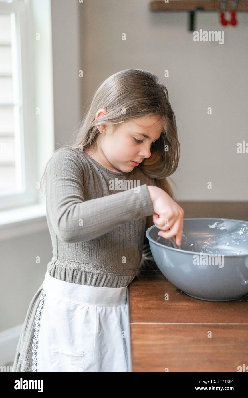 Ein Mädchen mischt Kekse in einer Schüssel und trägt eine Schürze Stockfoto