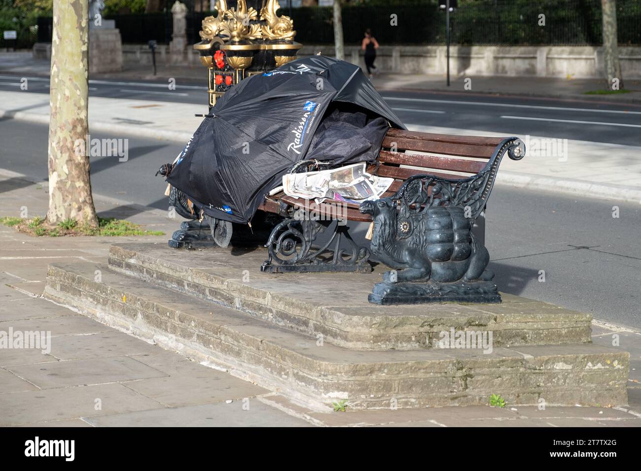 Ein provisorischer Schutz mit Regenschirmen auf einer Sitzbank bedeckt einen Obdachlosen auf den Straßen von London, Großbritannien Stockfoto