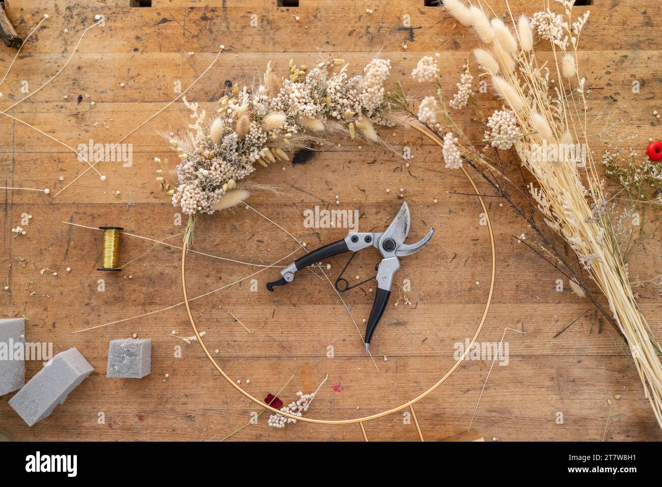 Overhead-Ansicht des Arbeitsplatzes eines Blumenhandels mit den Anfängen eines Kranzes, Werkzeugen und Materialien Stockfoto