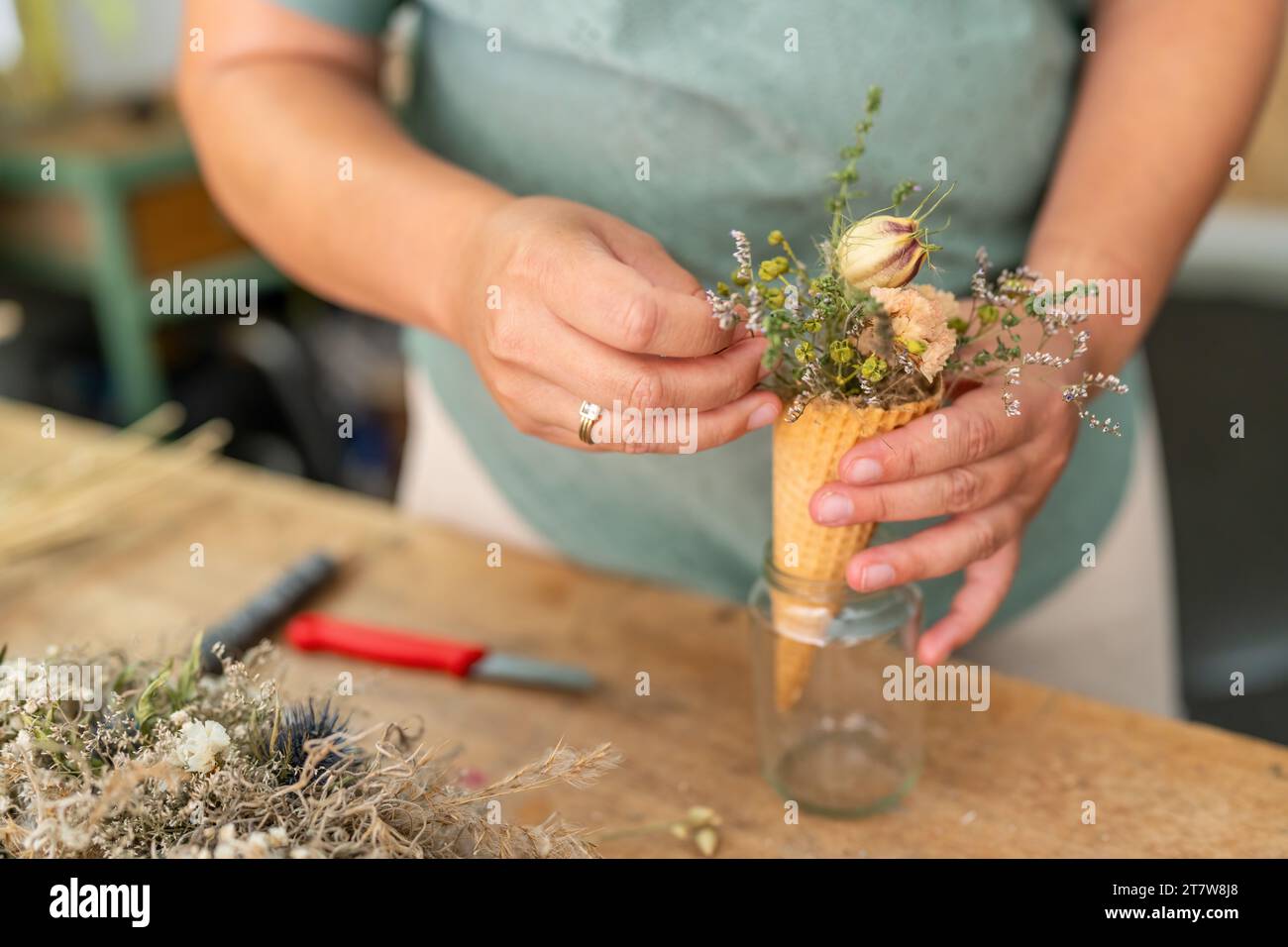Hände, die einen Strauß getrockneter Blüten in einem Eiskegel in ein Glas legen Stockfoto