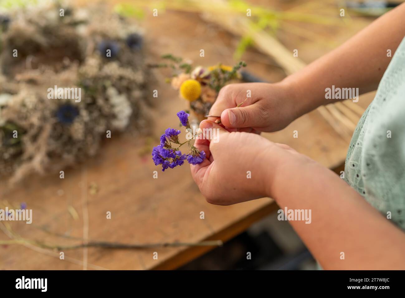 Floristin schneidet den Stamm einer getrockneten Blume mit einem Bastelmesser auf einem Holztisch in der Werkstatt Stockfoto