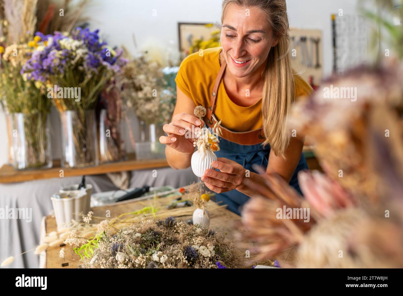 Floristin arrangiert eine kleine weiße Vase mit getrockneten Blumen in einer hellen Werkstatt Stockfoto