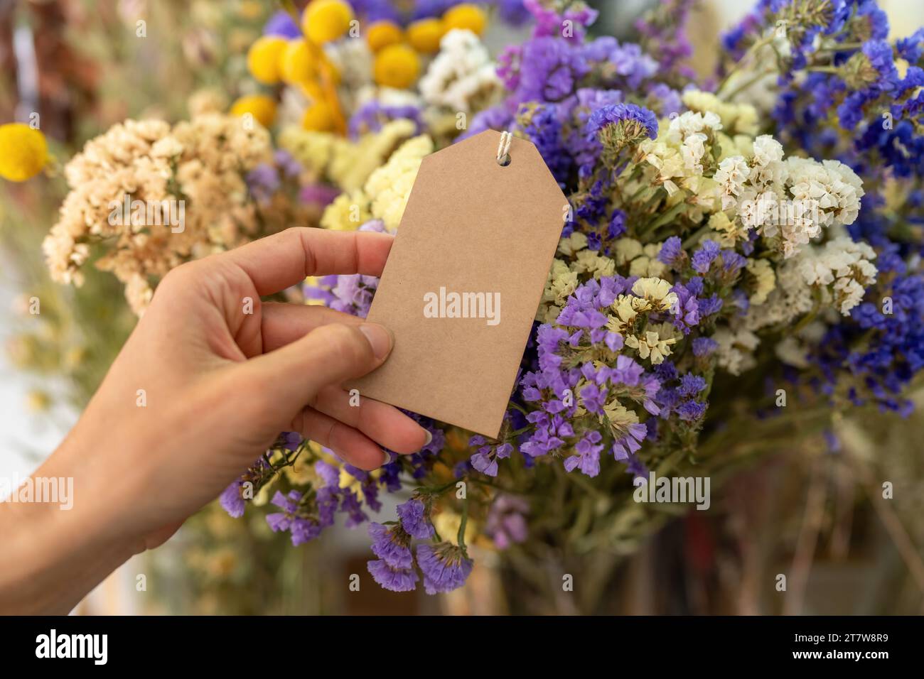 Halten Sie ein leeres braunes Etikett vor einem Strauß aus bunten getrockneten Blumen, mit Copyspace für Ihren individuellen Text. Stockfoto