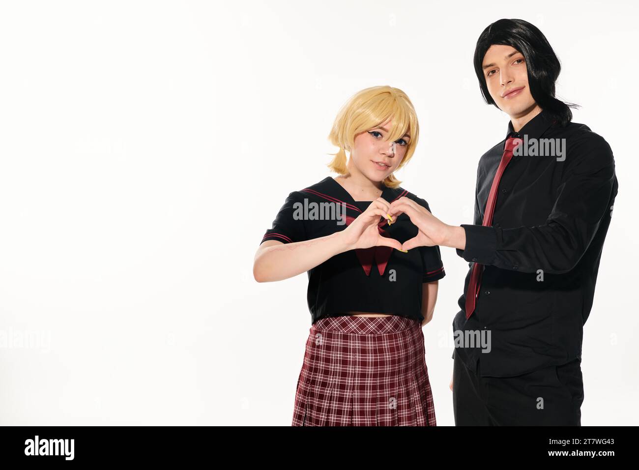 Cosplay-Paar in schwarzen und blonden Perücken mit Herzzeichen, mit Händen, die in die Kamera auf weiß schauen Stockfoto