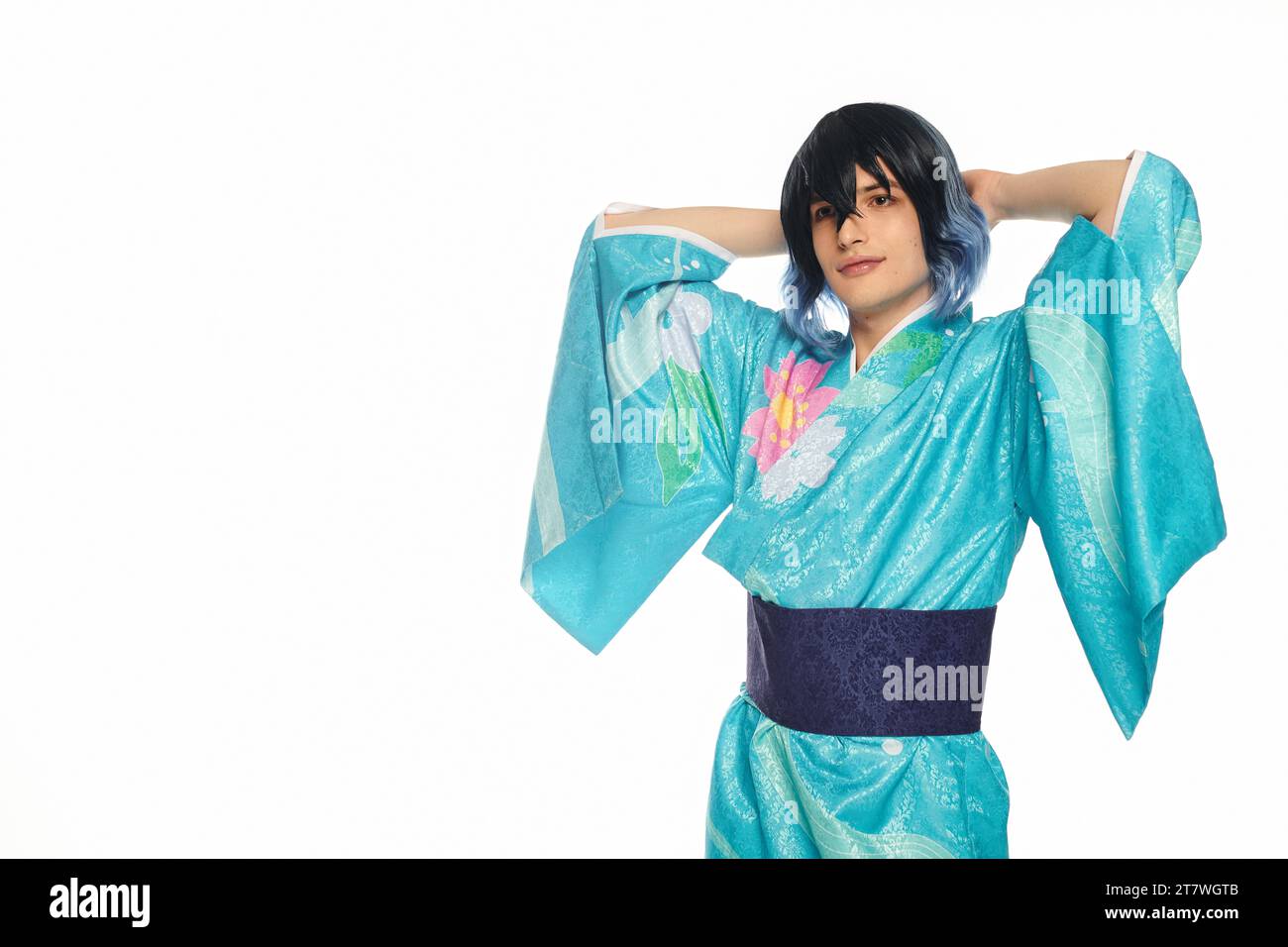 Junger Mann im blauen Kimono mit Händen hinter dem Kopf, der auf dem weißen, traumhaften Cosplayer in die Kamera schaut Stockfoto