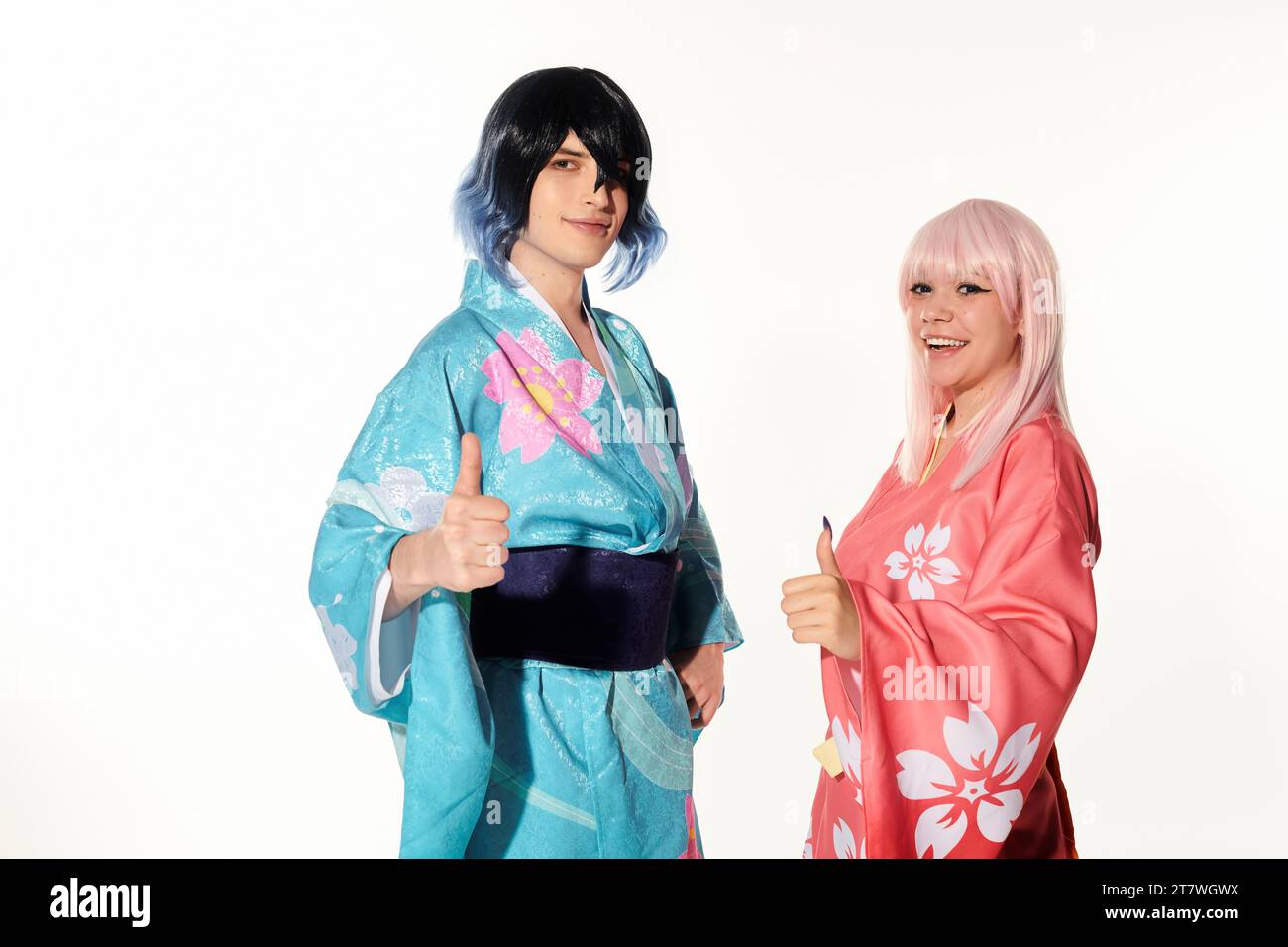 Anime-Paar in Perücken und Kimonos mit Daumen nach oben und Blick auf die Kamera auf weiß, Cosplay-Trend Stockfoto