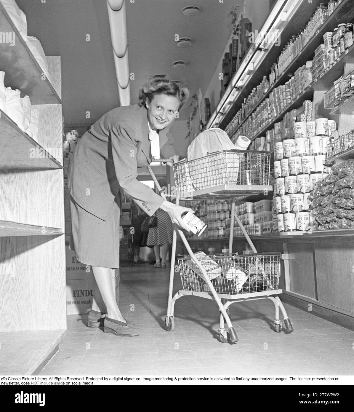 Shopping in den 1940er Jahren Eine Frau kauft in einem Selbstbedienungsladen ein. Sowohl die Idee des Self-Service als auch der Einkaufswagen kamen aus Amerika und zielten darauf ab, den Umsatz zu steigern. Der Kunde konnte sich die Lebensmittel aussuchen, in den Einkaufswagen legen und zur Kasse gehen. Zu dieser Zeit wurde diese Art des modernen Einkaufs in Schweden neu eingeführt. 1949. Kristoffersson Ref. AS47-1 Stockfoto