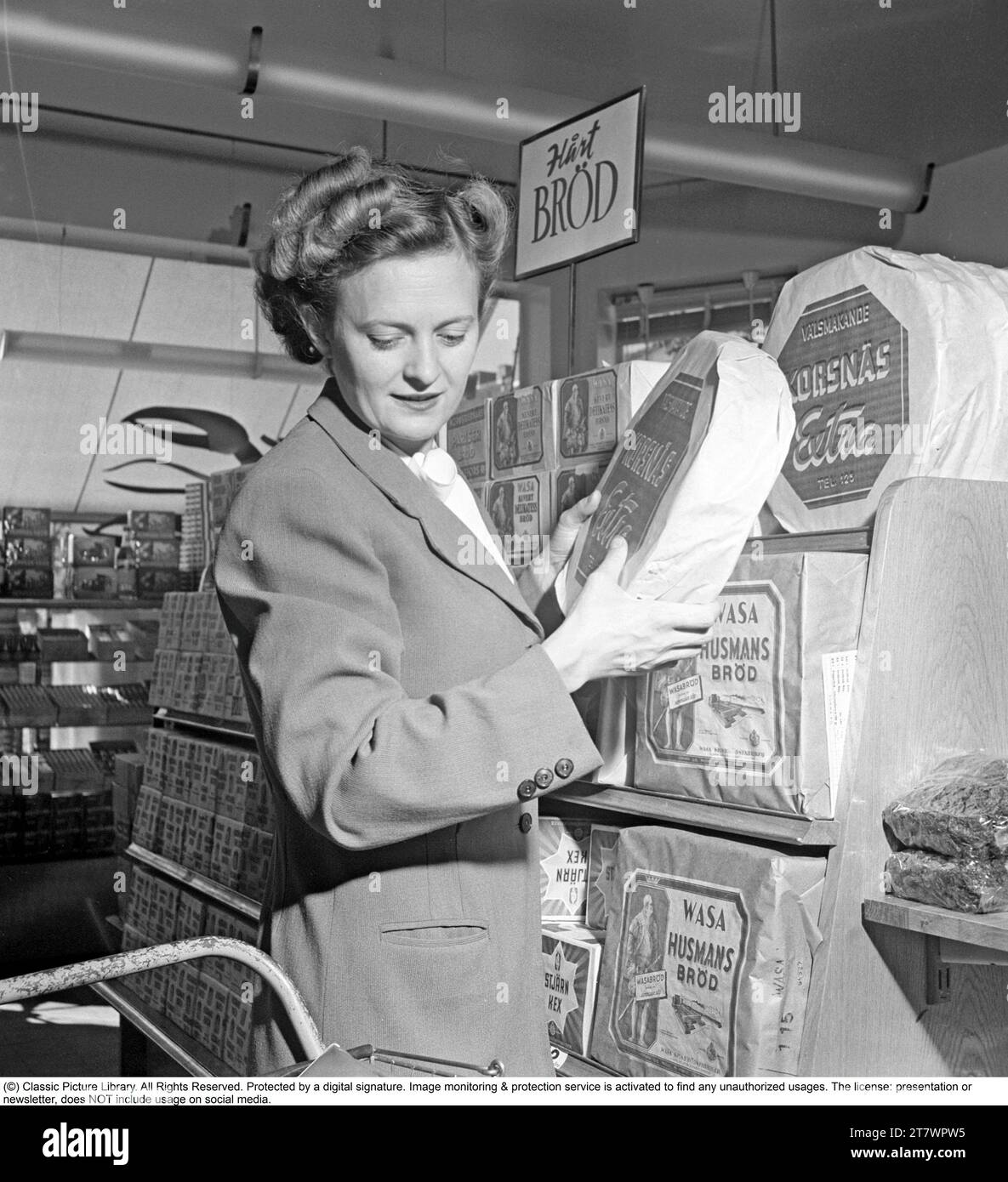 Shopping in den 1940er Jahren Eine Frau kauft in einem Selbstbedienungsladen ein. Sowohl die Idee des Self-Service als auch der Einkaufswagen kamen aus Amerika und zielten darauf ab, den Umsatz zu steigern. Der Kunde konnte sich die Lebensmittel aussuchen, in den Einkaufswagen legen und zur Kasse gehen. Zu dieser Zeit wurde diese Art des modernen Einkaufs in Schweden neu eingeführt. 1949. Kristoffersson Ref. AS47-3 Stockfoto