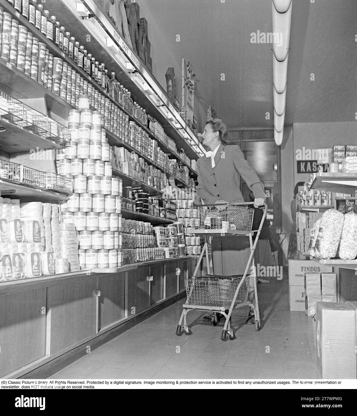 Shopping in den 1940er Jahren Eine Frau kauft in einem Selbstbedienungsladen ein. Sowohl die Idee des Self-Service als auch der Einkaufswagen kamen aus Amerika und zielten darauf ab, den Umsatz zu steigern. Der Kunde konnte sich die Lebensmittel aussuchen, in den Einkaufswagen legen und zur Kasse gehen. Zu dieser Zeit wurde diese Art des modernen Einkaufs in Schweden neu eingeführt. 1949. Kristoffersson Ref. AS47-6 Stockfoto