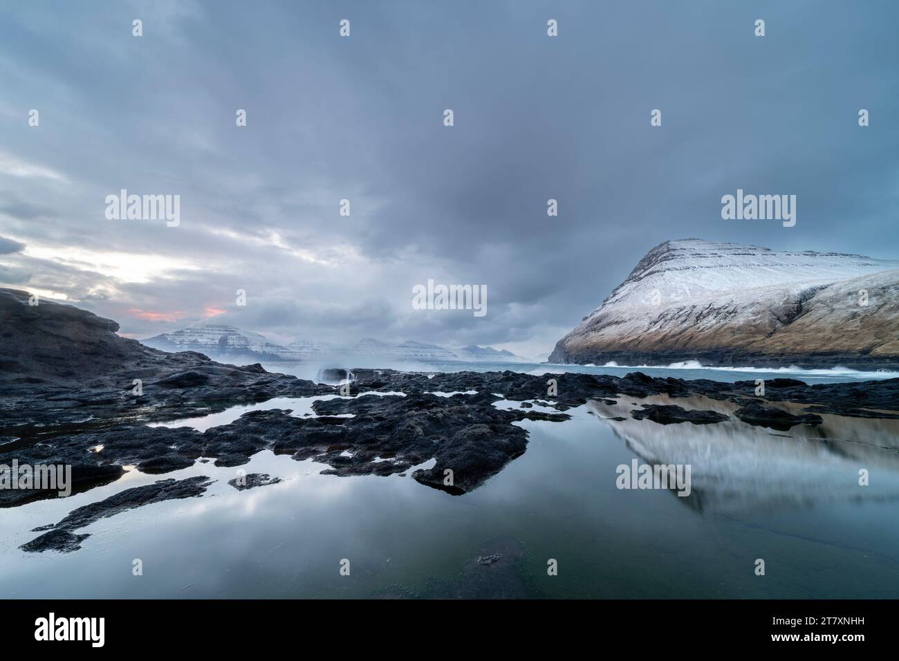 Schneebedeckte Berge und Felsbecken bei Ebbe, Gjogv Village, Eysturoy Island, Färöer Inseln, Dänemark, Europa Stockfoto