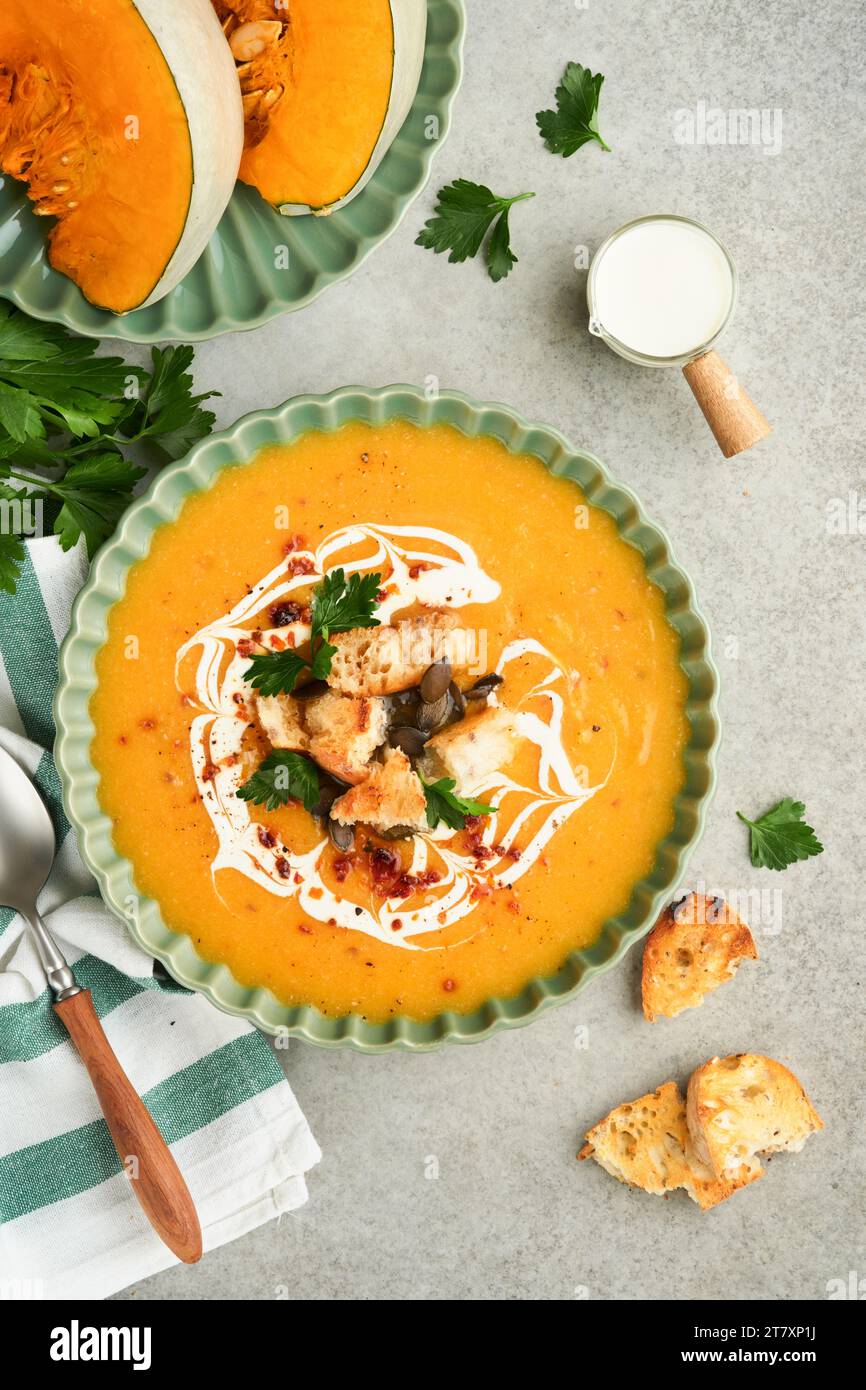 Kürbis-Karotten-Creme-Suppe mit Kräutern, Gewürzen und Samen in der Schüssel auf grauem Betontischhintergrund im rustikalen Stil. Thanksgiving traditionelles Autom Stockfoto