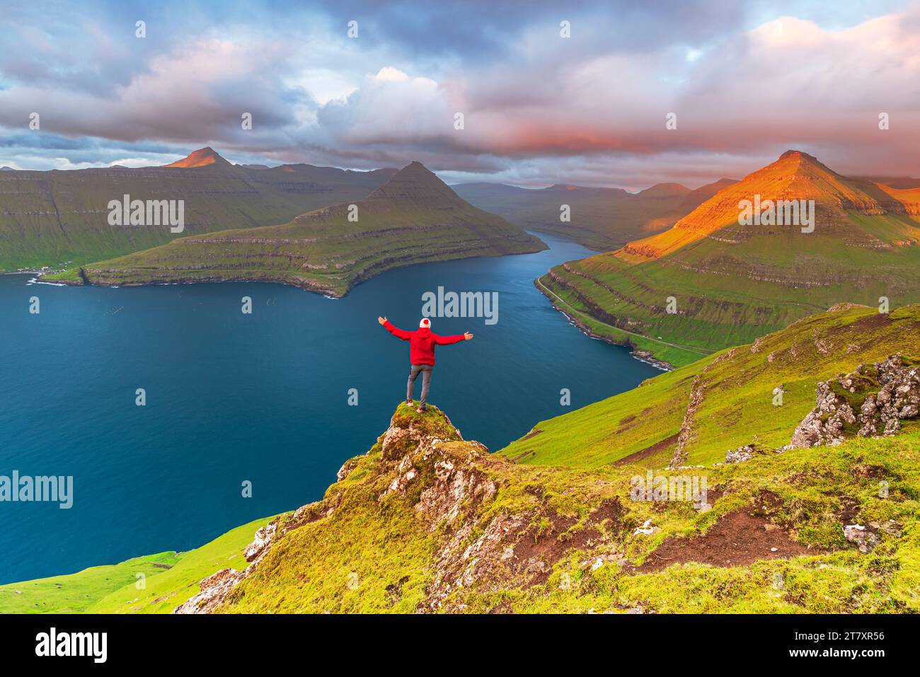 Glücklicher Wanderer steht auf der Klippe mit Blick auf den Fjord von Funningur, Eysturoy Island, Färöer Inseln, Dänemark, Europa Stockfoto