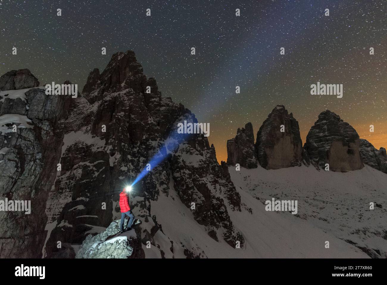 Der Mann mit Stirnlampe beleuchtet den Sternenhimmel über dem verschneiten Paterno und den drei Zinnen von Lavaredo, Sexten und Dolomiten Stockfoto