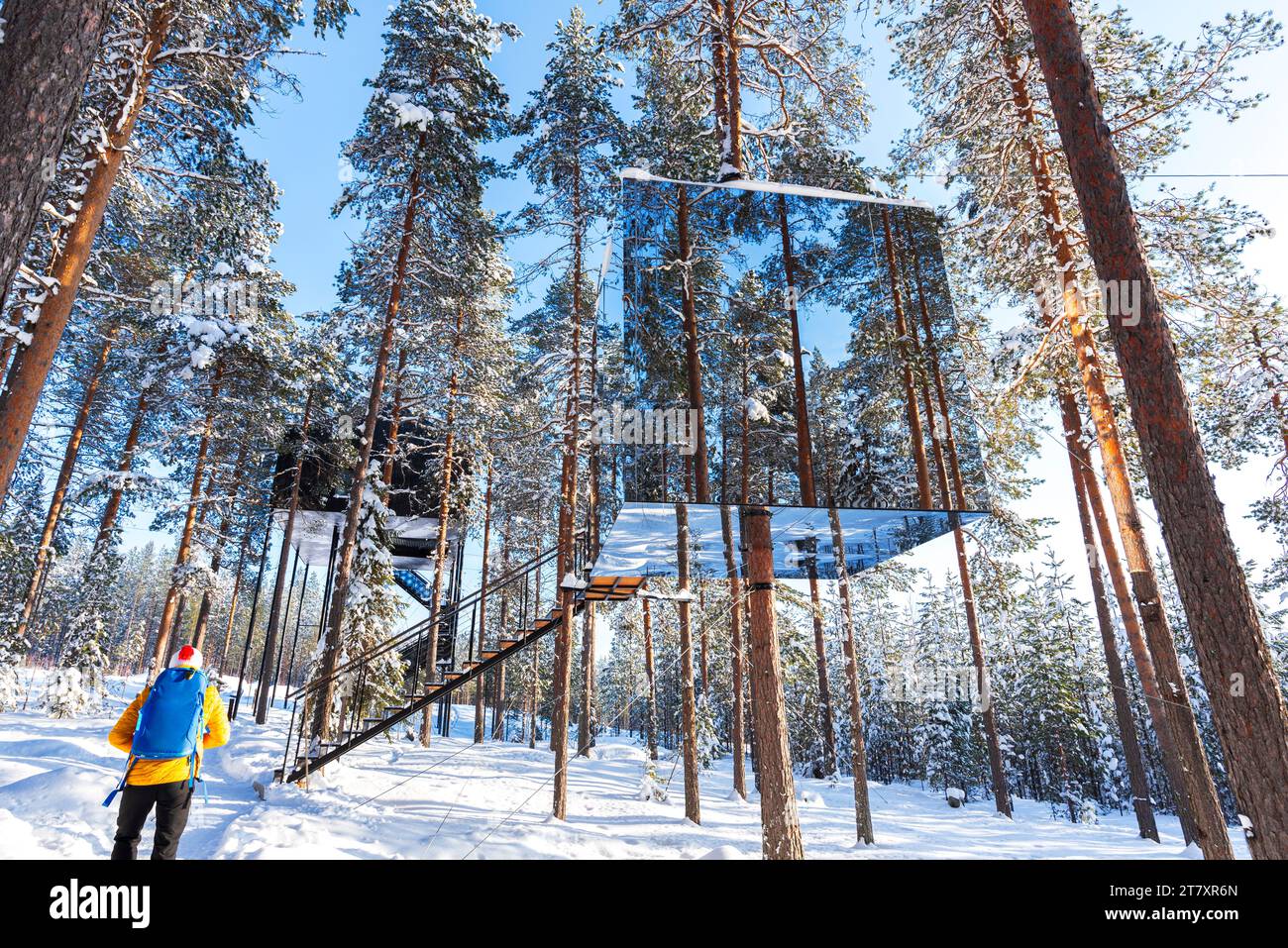 Blick auf einen Touristen, der den würfelförmigen Raum mit Spiegelwand in einem mit Eis und Schnee bedeckten borealen Wald bewundert, Tree Hotel, Harads, Lappland, Schweden Stockfoto