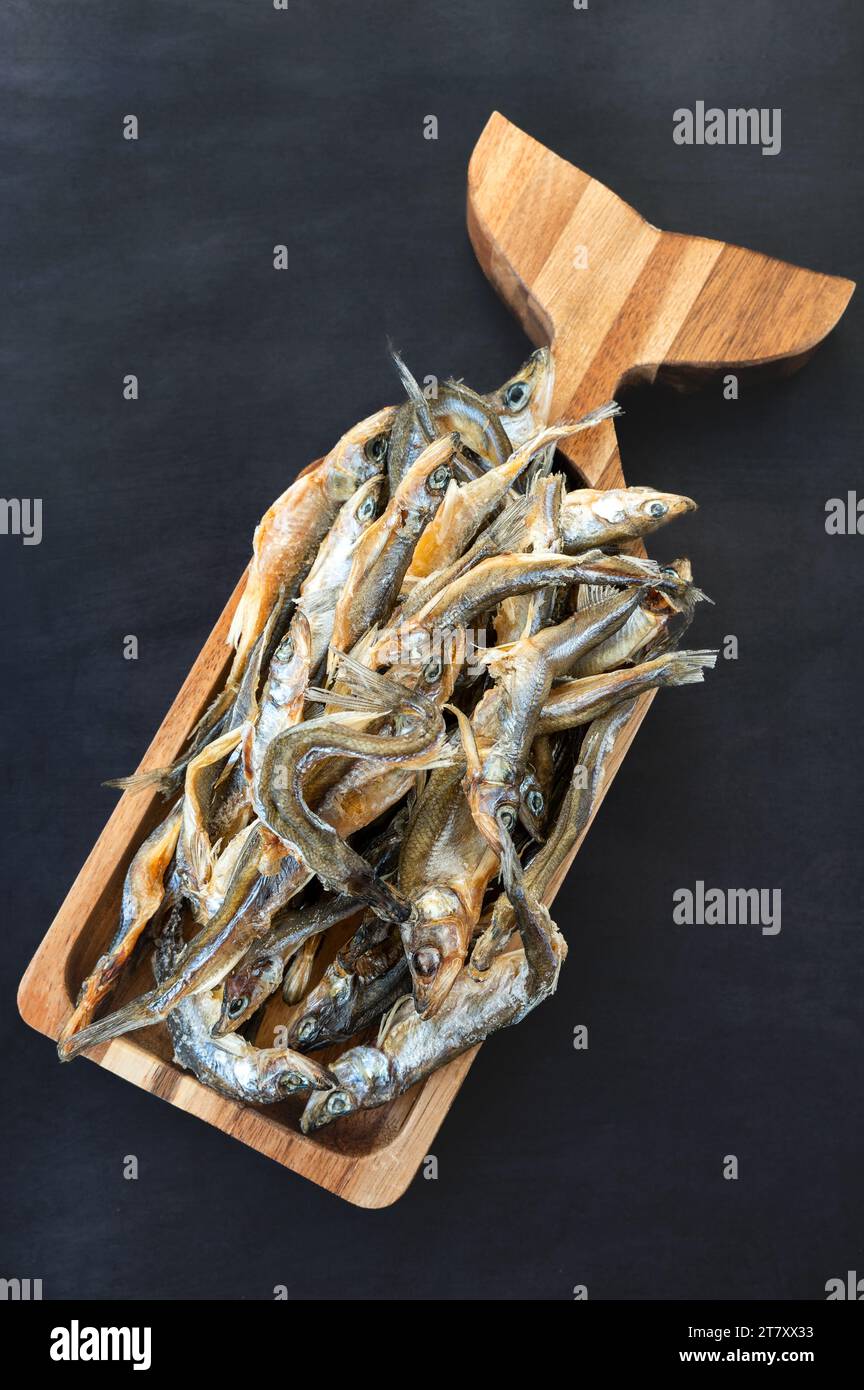 Klassische Vorspeise für Bier - getrocknete und gesalzene Sardellen, riechen, Sprotte auf einem Holzständer in Form eines Fisches auf dunklem Hintergrund. Bierkneipe. Stockfoto