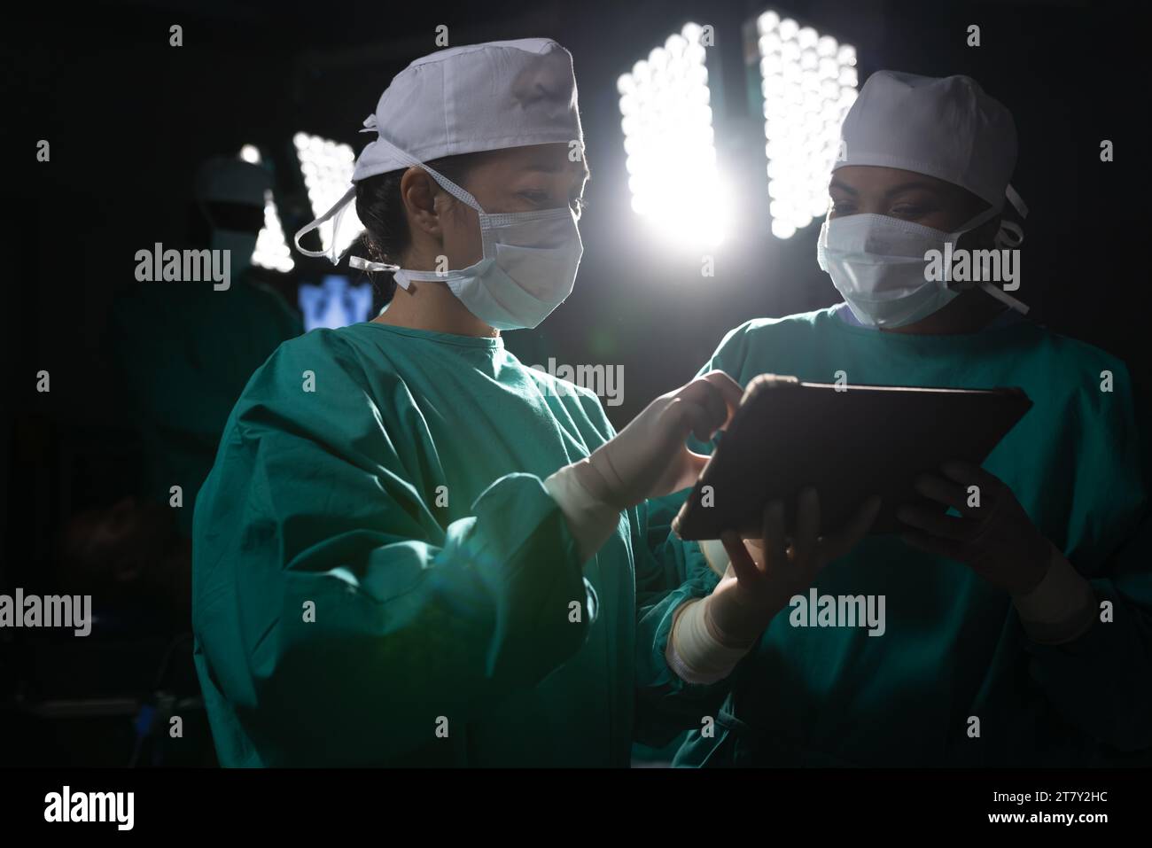 Diverse Chirurgeninnen diskutieren Arbeit mit Tablette im Operationssaal im Krankenhaus Stockfoto