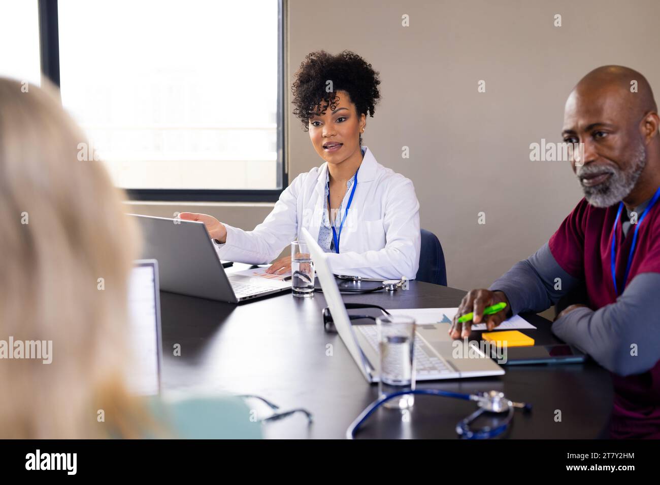 Glückliche, vielfältige männliche und weibliche medizinische Mitarbeiter mit Laptops, die sich bei Bürositzungen unterhalten Stockfoto