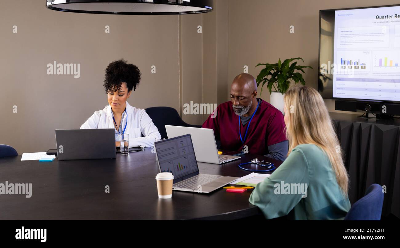 Diverse männliche und weibliche medizinische Mitarbeiter mit Laptops, die bei Bürositzungen arbeiten Stockfoto
