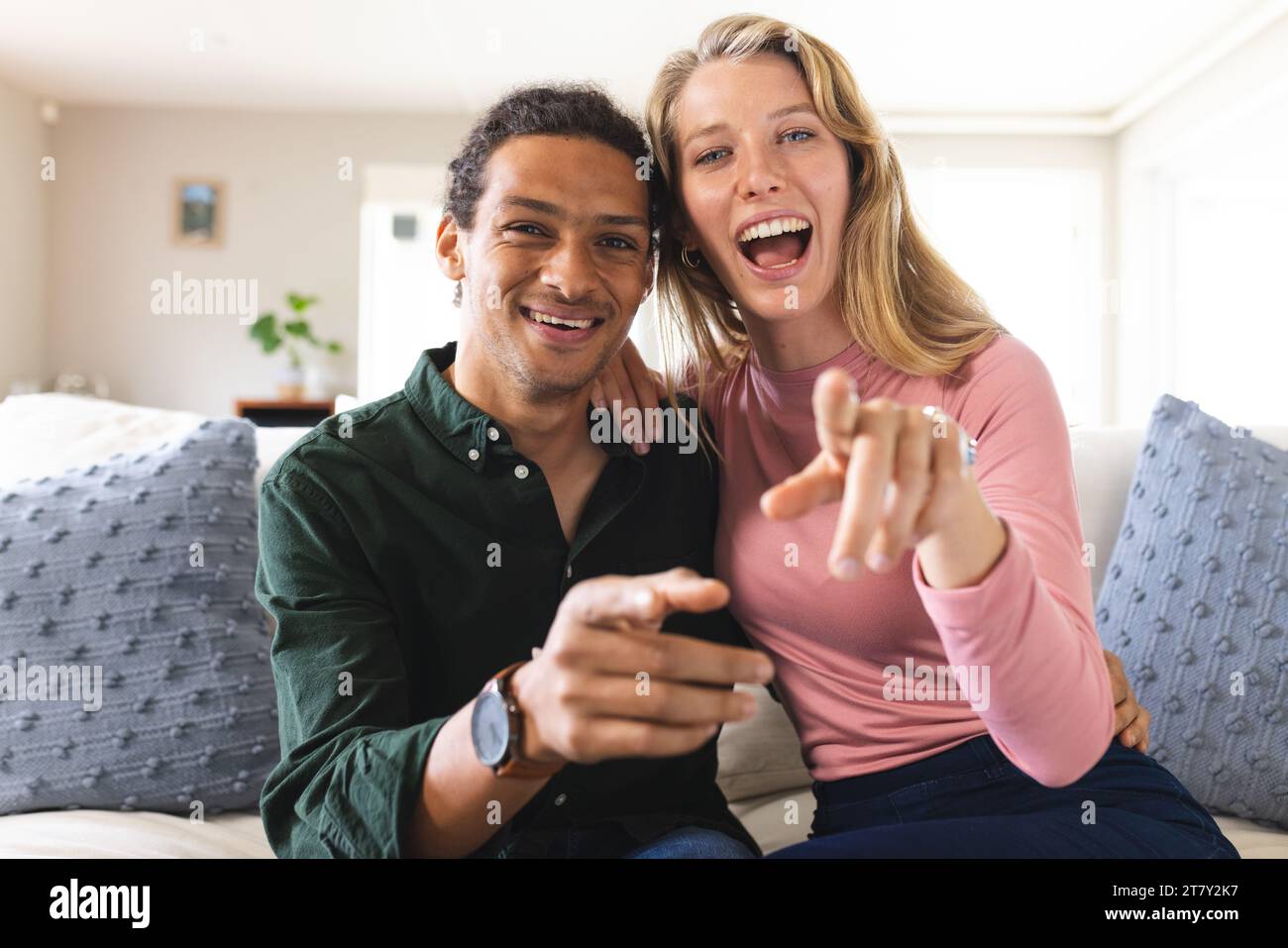 Glückliches, vielseitiges Paar mit Videoanruf und gestikuliertem Gesicht im sonnigen Wohnzimmer Stockfoto