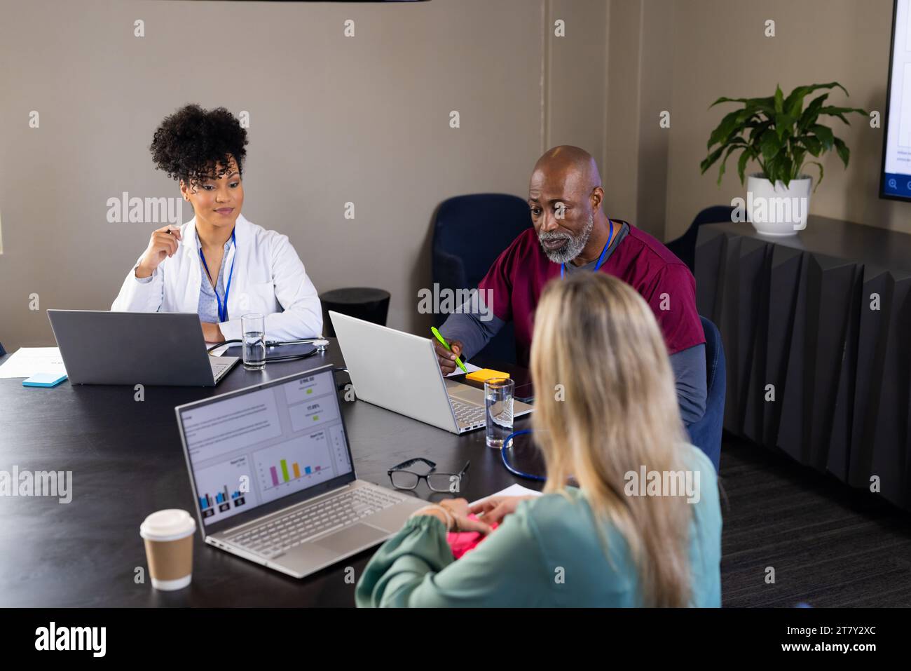 Glückliche, vielfältige männliche und weibliche medizinische Mitarbeiter mit Laptops, die sich bei Bürositzungen unterhalten Stockfoto