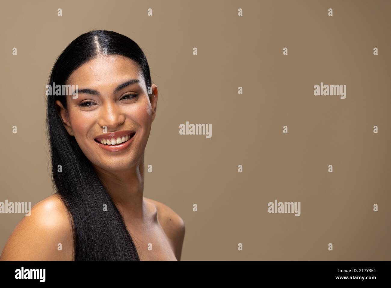 Porträt einer zweirassigen Frau mit dunklem Haar, lächelndem und natürlichem Make-up auf braunem Hintergrund Stockfoto