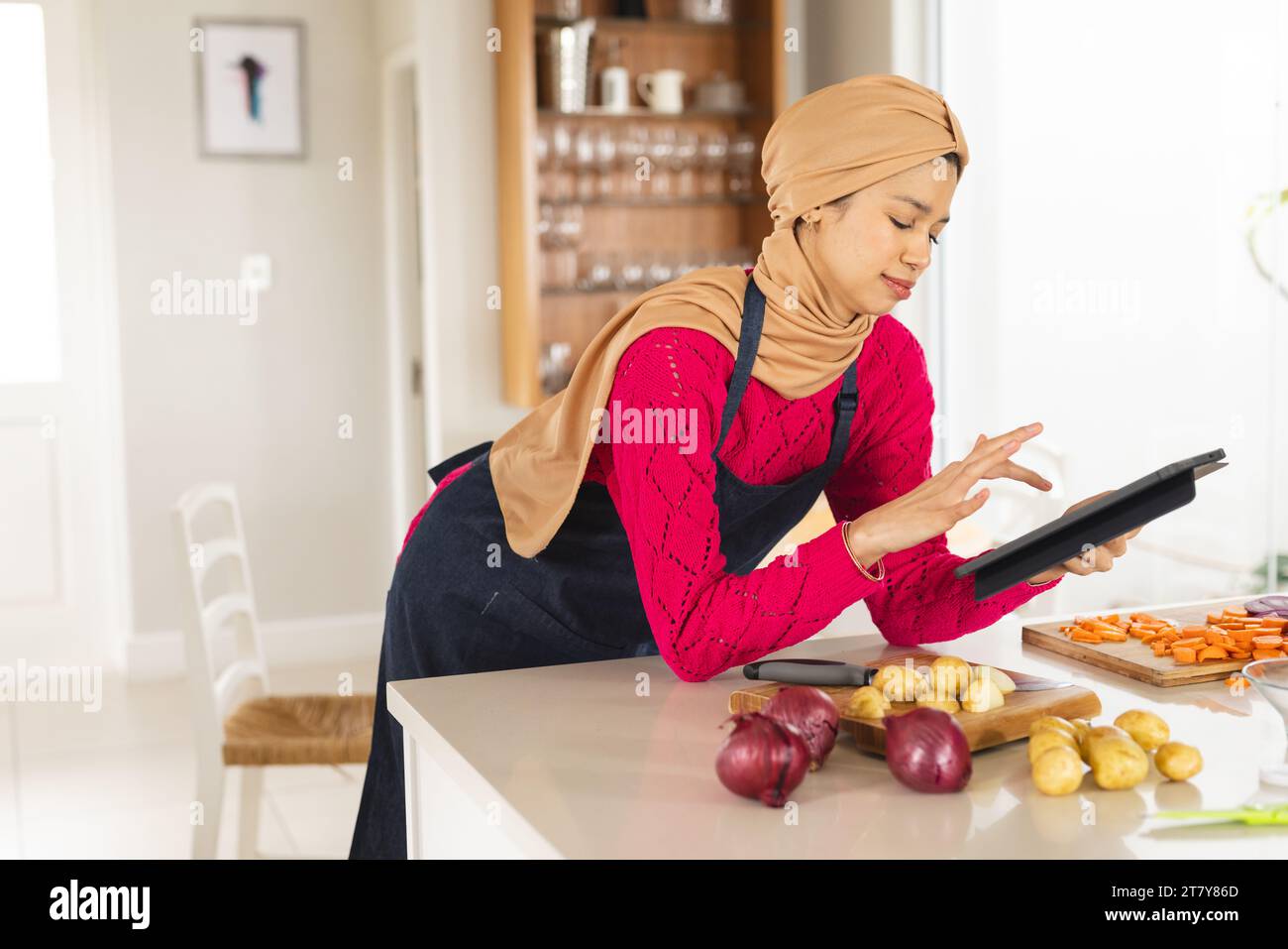 Birassische Frau in Hijab und Schürze mit Tablette in der Küche Stockfoto