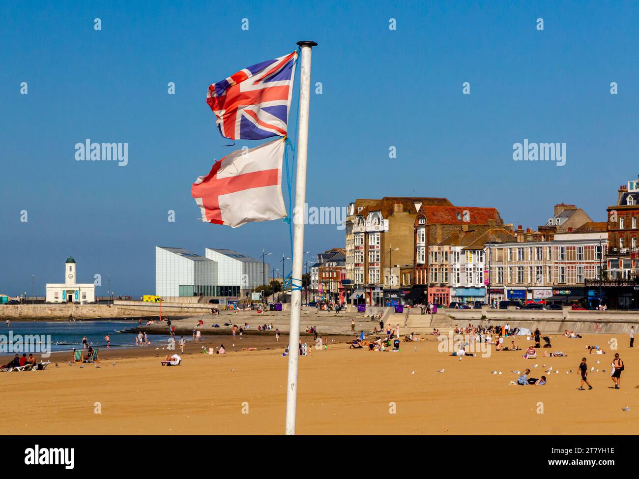 Sandstrand und Promenade in Margate, einem Badeort an der Küste von Kent im Südosten Englands, Großbritannien, mit zerrissenen englischen und britischen Flaggen an einem Pol. Stockfoto