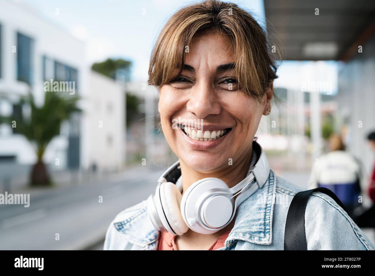 Glückliche Lateinfrau, die vor der Kamera lächelt, während sie am Busbahnhof in der Stadt wartet Stockfoto