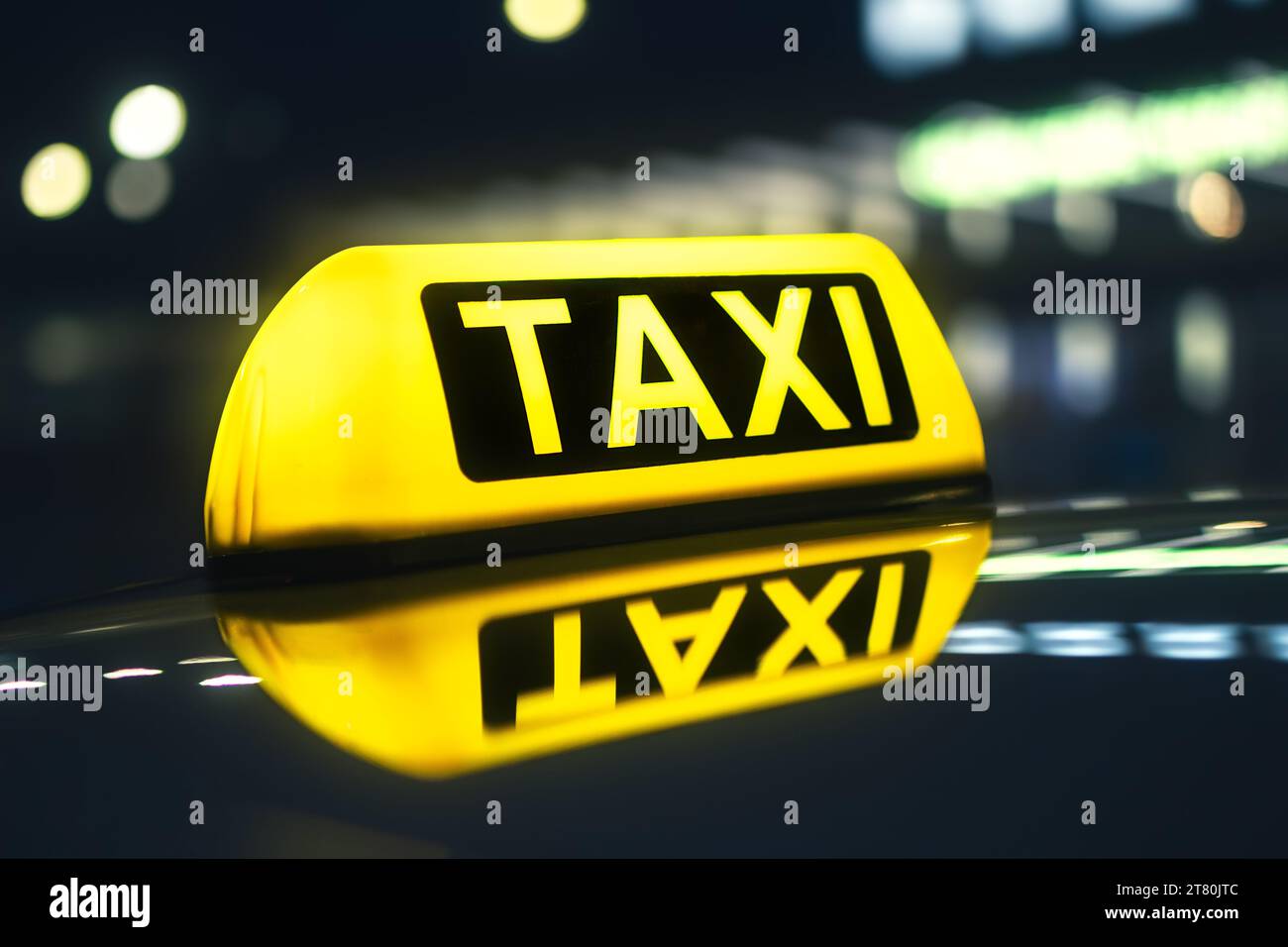 Selektiver Fokus auf gelbes Taxischild. Reflexion im Autodach gegen Neonlichter der Stadtstraße bei Nacht. Stockfoto