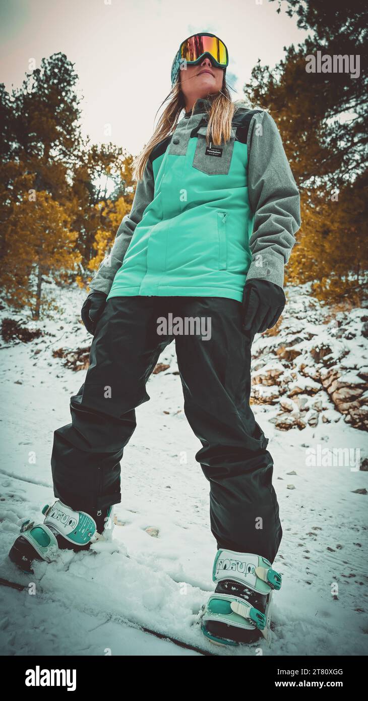 Eine Skifahrerin, die auf einem verschneiten Berg steht, eine hellblaue Skijacke trägt und bereit ist, auf die Pisten zu gehen Stockfoto